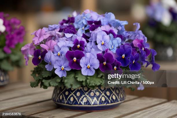 a bouquet of purple and blue flowers in a patterned ceramic pot on a wooden surface - pansy stock pictures, royalty-free photos & images