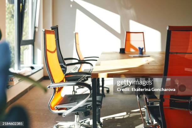 bright and modern meeting room with orange mesh chairs and wooden table. sunlight streaming through windows casting dynamic shadows. - office chair stock pictures, royalty-free photos & images