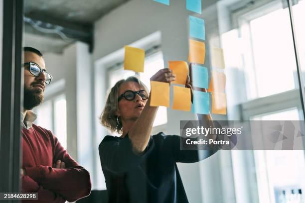uomini d'affari che usano post-it, discutono strategie e brainstorming in ufficio - spremersi le meningi foto e immagini stock
