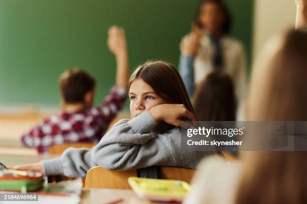nachdenkliche schülerin unter ihren klassenkameraden in der grundschule. - schulkind stock-fotos und bilder