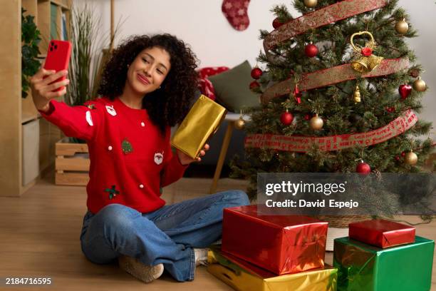young woman taking selfie showing christmas gift next to christmas tree - christmas zoom stock pictures, royalty-free photos & images