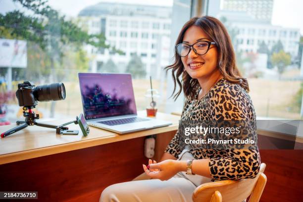 una joven creadora de contenido graba un video sobre la bolsa de valores en línea en un moderno entorno de café - micromecenazgo fotografías e imágenes de stock