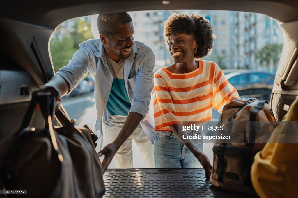 Couple loading luggage into car in urban setting.