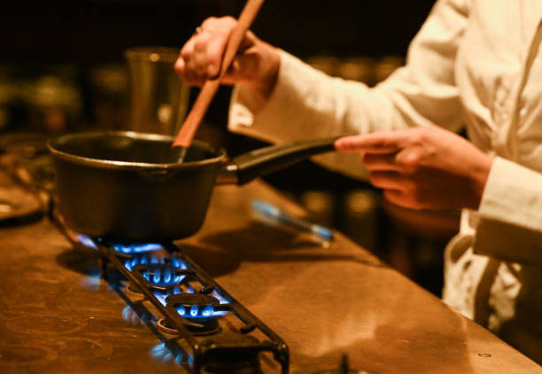 Staff member melting chocolate over natural gas burners on a stove in a Krakow cafe, showcasing the role of natural gas in professional cooking, seen...