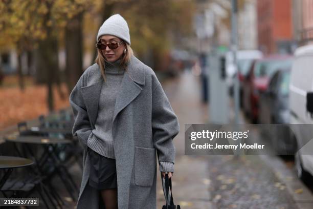 Sonia Lyson is seen wearing a light grey knit beanie from Le Bonnet; chunky silver hoop earrings; oval sunglasses with Havana frame and silver...