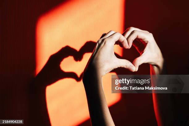 a heart made of hands and its shadow on a bright yellow background on a sunny day, a symbol of love. - gesto con la mano foto e immagini stock