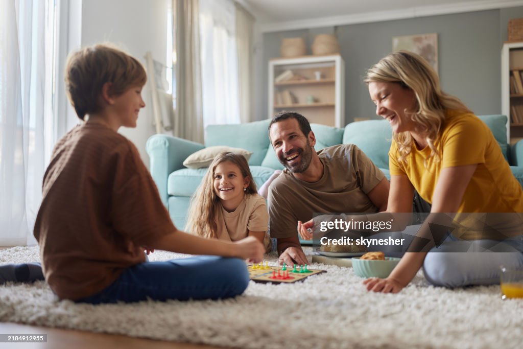 Happy parents and their kids playing Ludo on carpet at home.