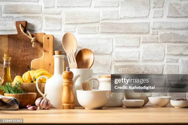 kitchen table with white crockery and wooden utensils. copy space on white bricks wall at background - keukengereedschap stockfoto's en -beelden