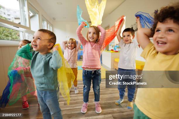 los niños en la sala de juegos bailan con bufandas en las manos - cuidado infantil fotografías e imágenes de stock
