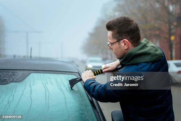 man scraping snow off car windshield - voorruit stockfoto's en -beelden