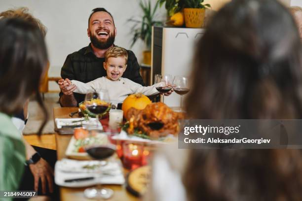 father playing with son holding his hands while both laughing on thanksgiving celebration - boy sitting at table stock pictures, royalty-free photos & images