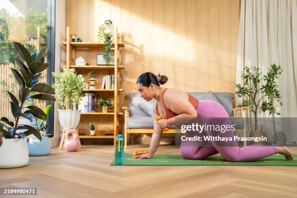 woman practicing fitness with dumbbells at home in bright room - entrenamiento-sin-material fotografías e imágenes de stock