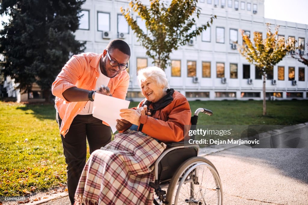 Old people in wheelchair care outdoor by young adult volunteer reading prescription together and explaining which medicine to take