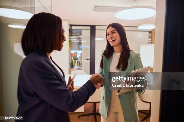 two businesswomen shaking hands in modern office setting - impact stock pictures, royalty-free photos & images