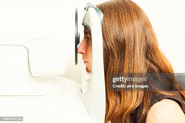 side view of a young woman sitting in an optician's office having a retinal examination. - astigmatismo imagens e fotografias de stock
