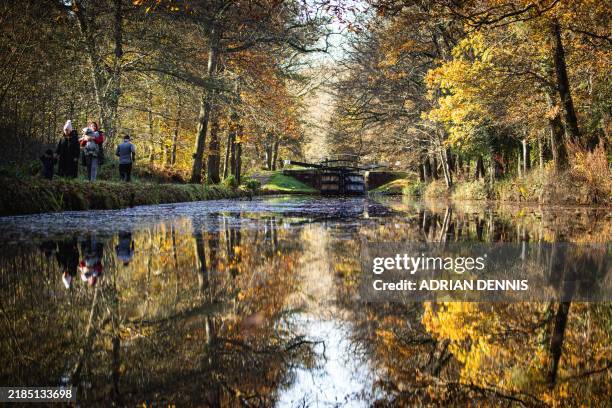 Pedestrians walk along the Basingstoke Canal, on an autumn day as the nature surrounding them is reflected in the water near Pirbright, west of...