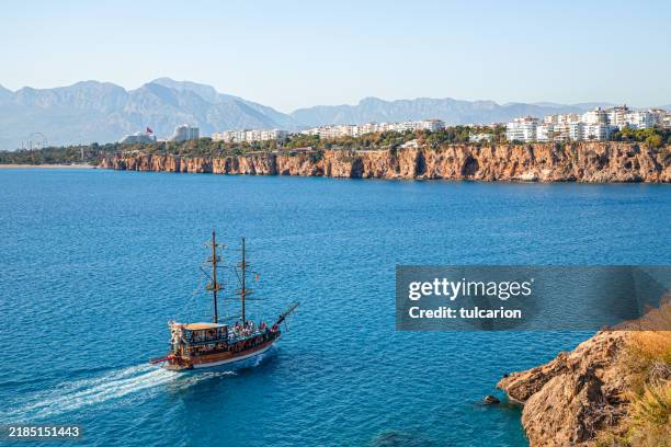 yacht pirate tour boat sailing along rugged rock shore in antalya’s mediterranean sea - antalya province stock pictures, royalty-free photos & images