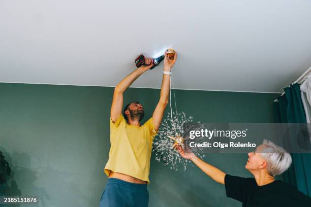 repairman drilling place for light fixture while female owner holding chandelier - installing ceiling light fixture stock pictures, royalty-free photos & images
