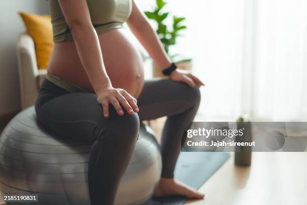 close-up shot of pregnant woman sitting on a fitness ball relaxed at home. - pregnancy yoga ball stock pictures, royalty-free photos & images