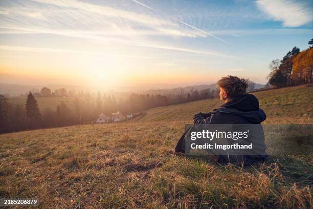 teenage boy looking at the sunset in the autumn hills - staring stock pictures, royalty-free photos & images