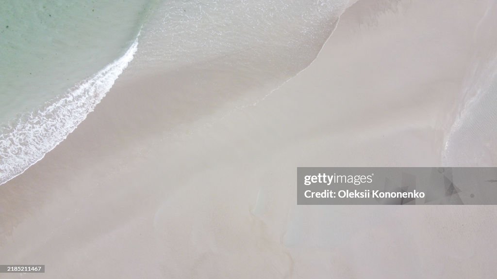 Sandy seashore, top view. Minimalistic seascape, a copy space. Wet sand. Natural background, texture. Peaceful beach background, sand and sea water. Ocean coast.