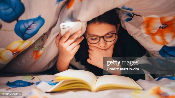 girl reading a book under blanket and lights with lantern from her phone - flashlight stock pictures, royalty-free photos & images