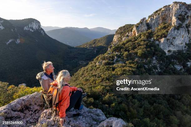 mature couple sit on edge of cliff above hills and forest - environmentalist stock pictures, royalty-free photos & images