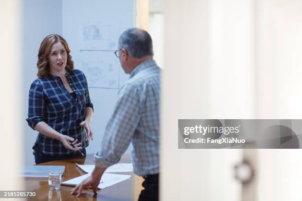 mid adult woman discusses plans explaining in meeting at table with senior man colleague teamwork in design office - communication problems stock pictures, royalty-free photos & images