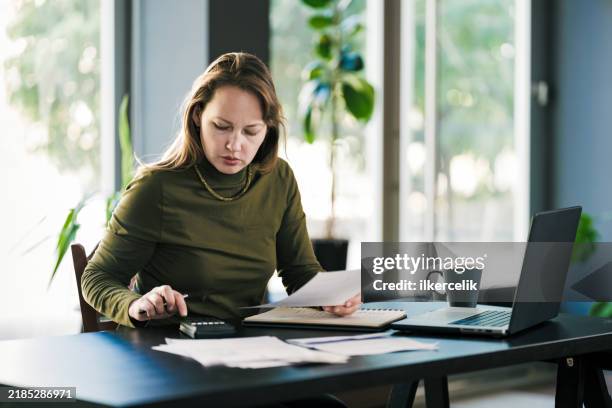 woman reviewing paper financial statements at home - woman calculator stock pictures, royalty-free photos & images