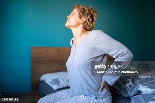 a woman holding her back in discomfort due to pain - lower back stock pictures, royalty-free photos & images
