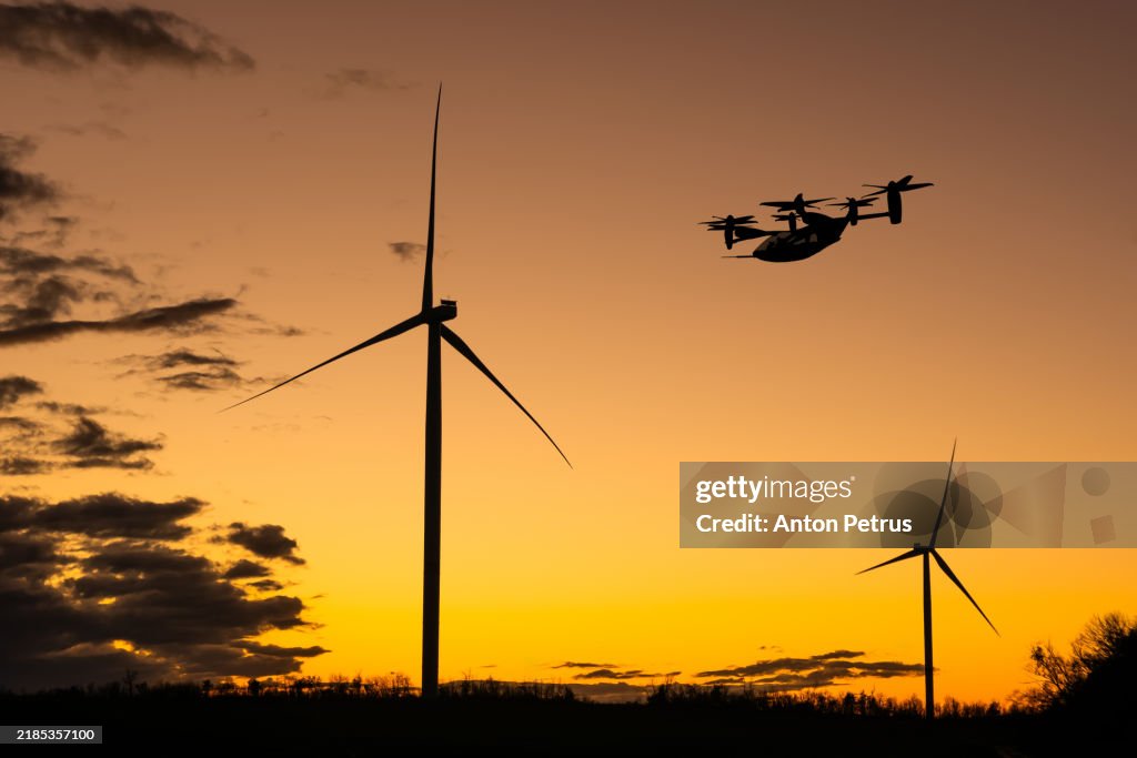 Futuristic air transport over wind turbines at sunset