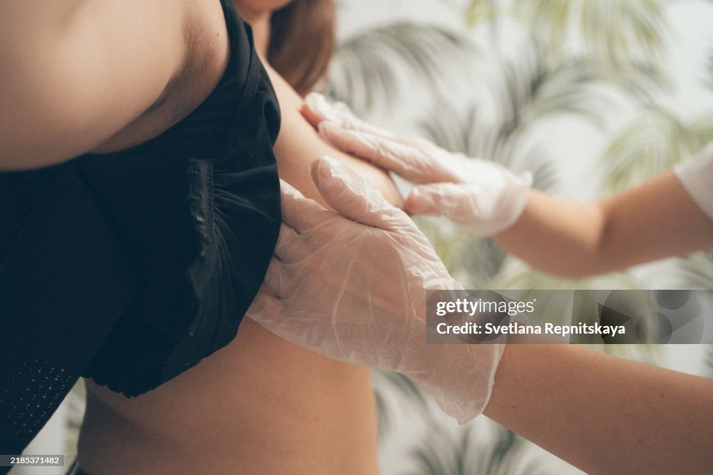 Female doctor surgeon in surgical gloves examines the stitches of a patient after plastic surgery, mammoplasty, breast augmentation