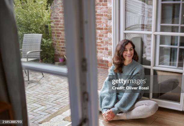 smiling brunette woman sitting on the floor by the patio door at home - natürlicher zustand stock-fotos und bilder