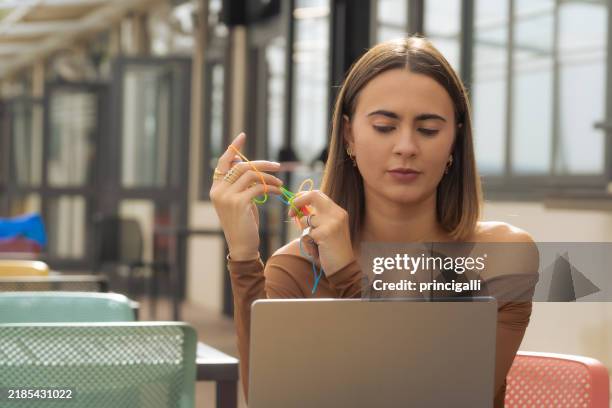 young woman at work with a computer using objects, rubber bands, toys, and assistive devices for concentration. - technology distraction stock pictures, royalty-free photos & images