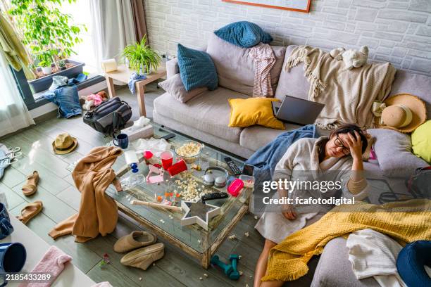 tired woman in bathrobe, eyes closed sitting on the floor of a messy living room - rommelig stockfoto's en -beelden