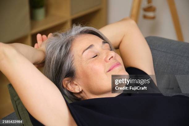 relaxed mature woman resting on sofa with hands behind head - hands behind head stock pictures, royalty-free photos & images
