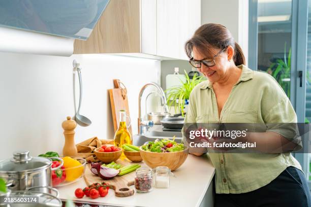 une femme détendue apprécie dans la cuisine de préparer une salade fraîche et saine pour le déjeuner - cuisine méditerranéenne photos et images de collection