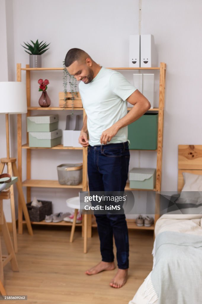 Young man buttoning jeans in modern minimalist bedroom