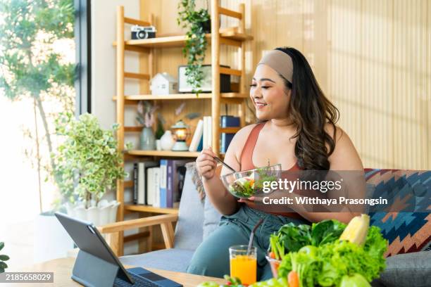 woman enjoys healthy salad while watching online content at home - pflanzliche ernährung stock-fotos und bilder