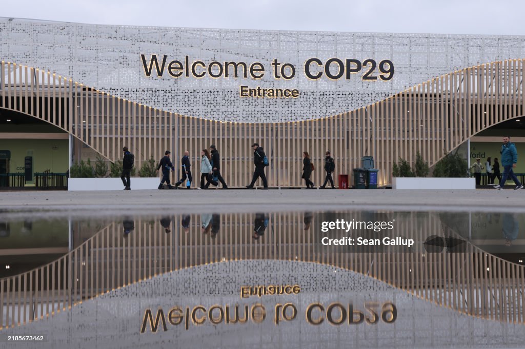 Cop29 Conference participants are reflected in a puddle as they arrive on ...