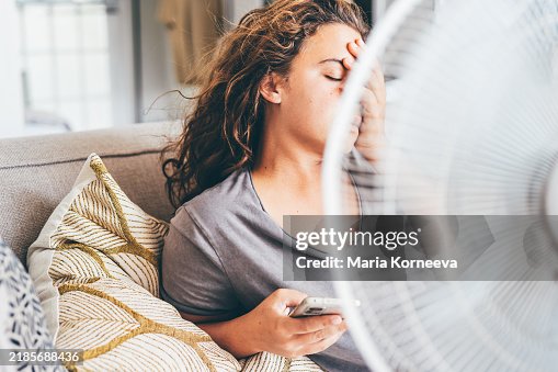 Happy contented woman using electric fan at home enjoying fresh air on hot summer day. Happy contented woman using electric fan at home enjoying fresh air on hot summer day.
