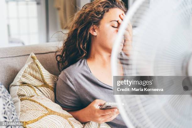happy contented woman using electric fan at home enjoying fresh air on hot summer day. - feber bildbanksfoton och bilder