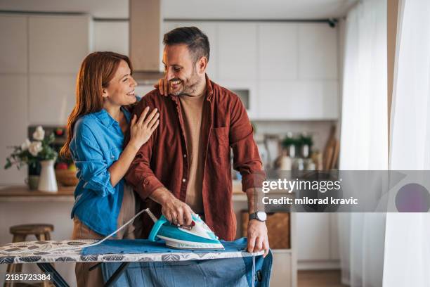 un marido y una mujer alegres están planchando mientras la cocina es visible en el fondo. - tarea doméstica fotografías e imágenes de stock