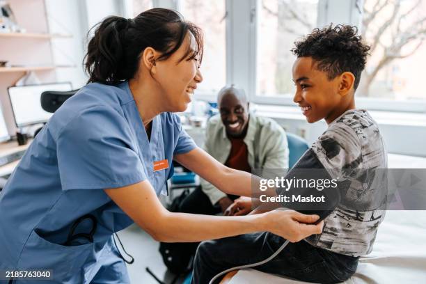 happy female pediatrician checking boy's blood pressure in examination room - pédiatre photos et images de collection