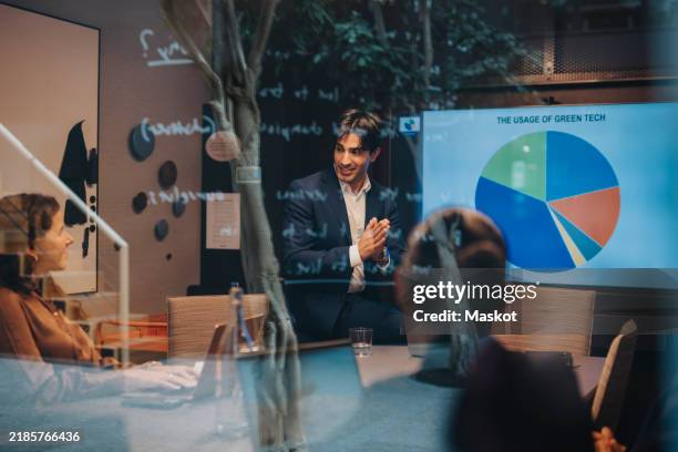 young male entrepreneur pitching female colleagues during meeting in board room - sustainable business stock pictures, royalty-free photos & images
