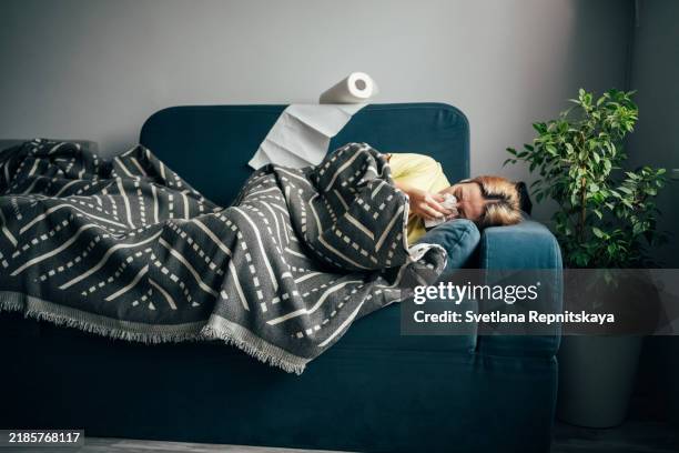 sick woman blows her nose into a napkin while lying on the sofa - flu virus stock pictures, royalty-free photos & images