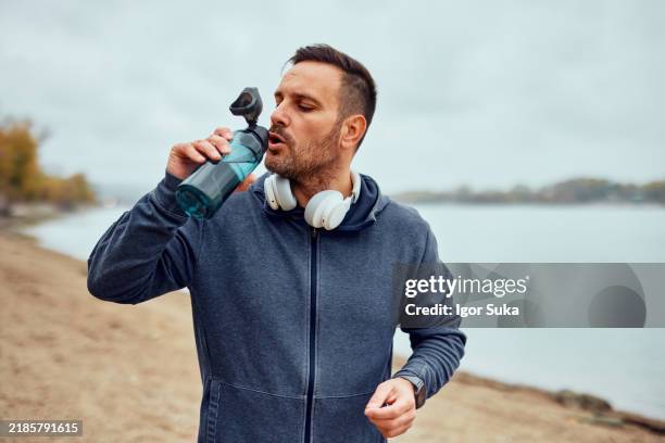 mann macht eine pause und trinkt wasser am strand - energydrink stock-fotos und bilder