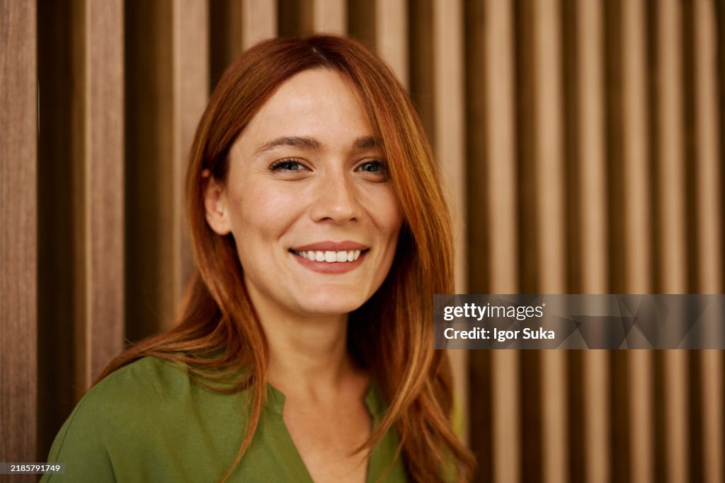 Confident Woman Smiling in Green Blouse Against Wooden Background