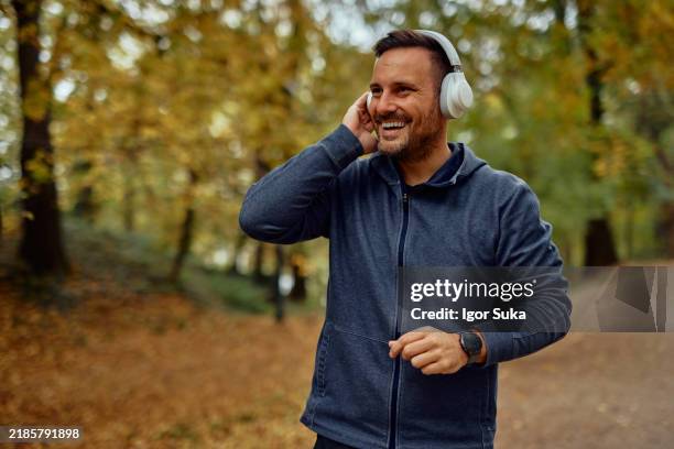 smiling man enjoying music with headphones in autumn park - white jacket stock pictures, royalty-free photos & images