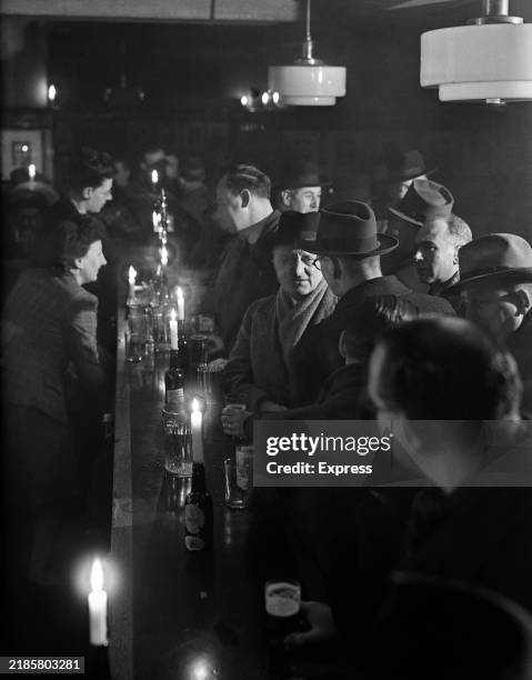 Customers in a pub lit by candlelight during the coal shortage blackout, London, February 11th 1947.